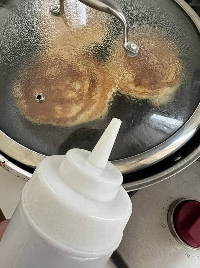 adding a few drops of water creates steam under a lid to raise the temperature of the pancakes so the additions don't weight heavy into the pancake batter and prevent the middle from cooking, the steam will increase the temperature making the pancakes cook quicker
