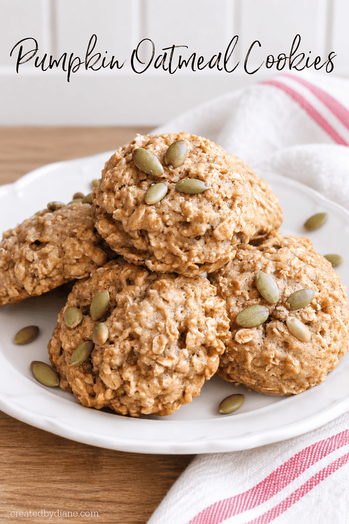 pumpkin oatmeal cookies on a white plate with pepitas on top, on a wood counter top, white backsplash and a white dish towel with red stripe,