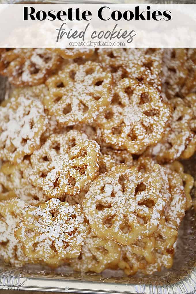 a tray full of fried rosette cookies dusted with powdered sugar, they look like lacy snowflakes