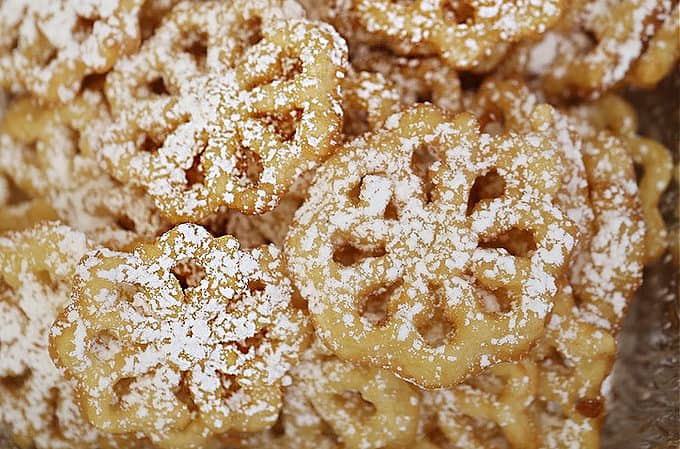 a tray full of fried rosette cookies dusted with powdered sugar, they look like lacy snowflakes