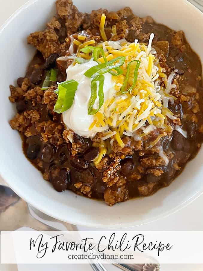 My FAVORITE Chili Recipe from createdbydiane.com white bowl of chili topped with cheese, sour cream and green onion