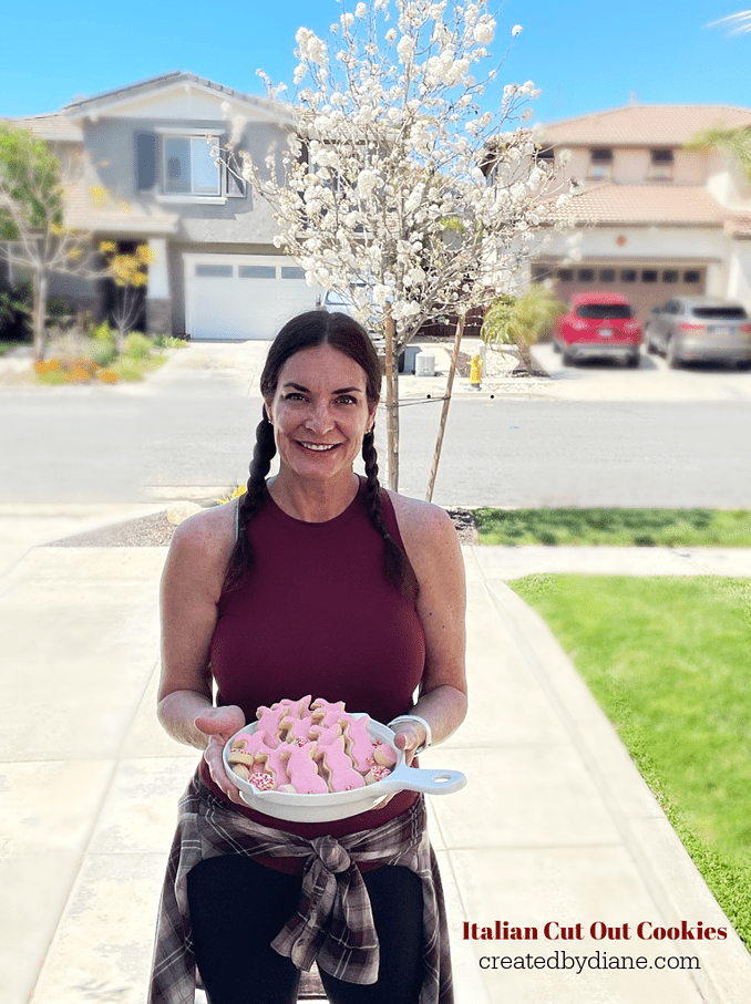 Italian Cut Out Cookies.... Easter Bunny Cookies In a white dish with Diane from createdbydiane.com holding them with a flowering white pear tree behind