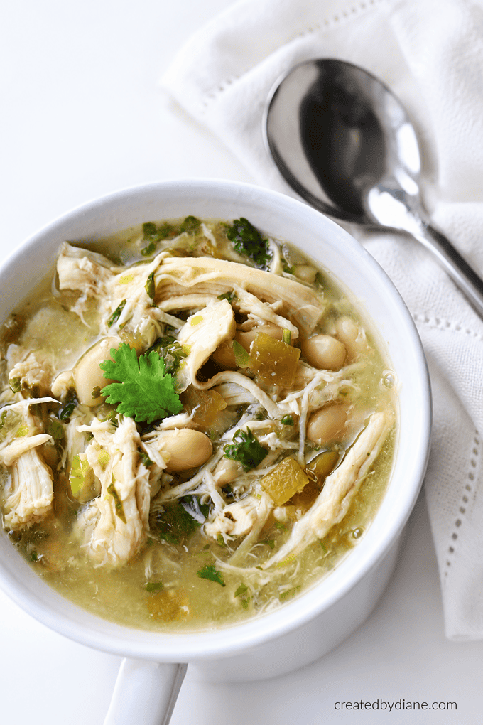WHITE CHILI with lot so fgreens to mkae it the best chicken chili recipe at createdbydiane.com green chicken chili in a white mug tender chicken, with cilantro and a light green sauce that tastes flavorful and bright with the citrus kick