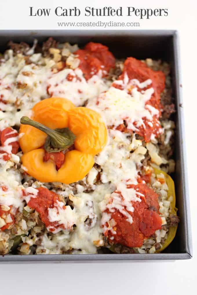 square baking dish with yellow and red stuffed peppers with cauliflower and ground beef topped with sauce and cheese