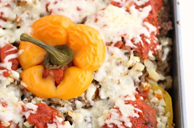 square baking dish with yellow and red stuffed peppers with cauliflower and ground beef topped with sauce and cheese