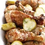 sliced pickles with dill on crispy chicken legs in a white dish