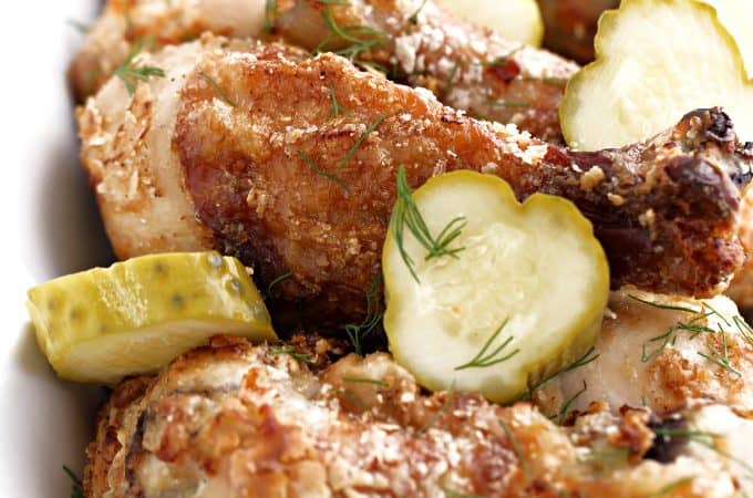 sliced pickles with dill on crispy chicken legs in a white dish