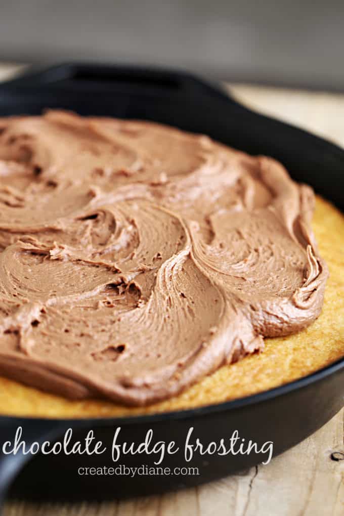 chocolate fudge frosting on a vanilla skillet cake in a cast iron skillet on a wood table