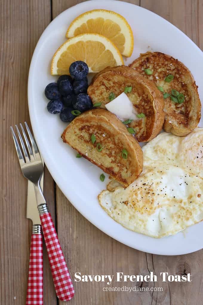 white oval plate with savory french toast, fried eggs, blueberries, orange slices and forks with red gingham checks