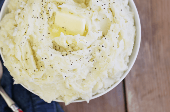 ta bowl of freshly mashed potatoes cooked in the Instant Pot with a pat of butter, melted, salt and pepper with a denim napkin and red and white check spoon