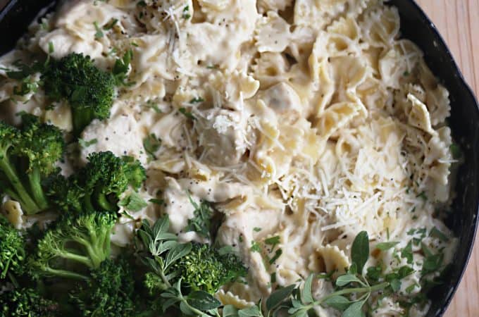 cast iron skillet loaded with chicken pasta and alfredo sauce topped with spinach