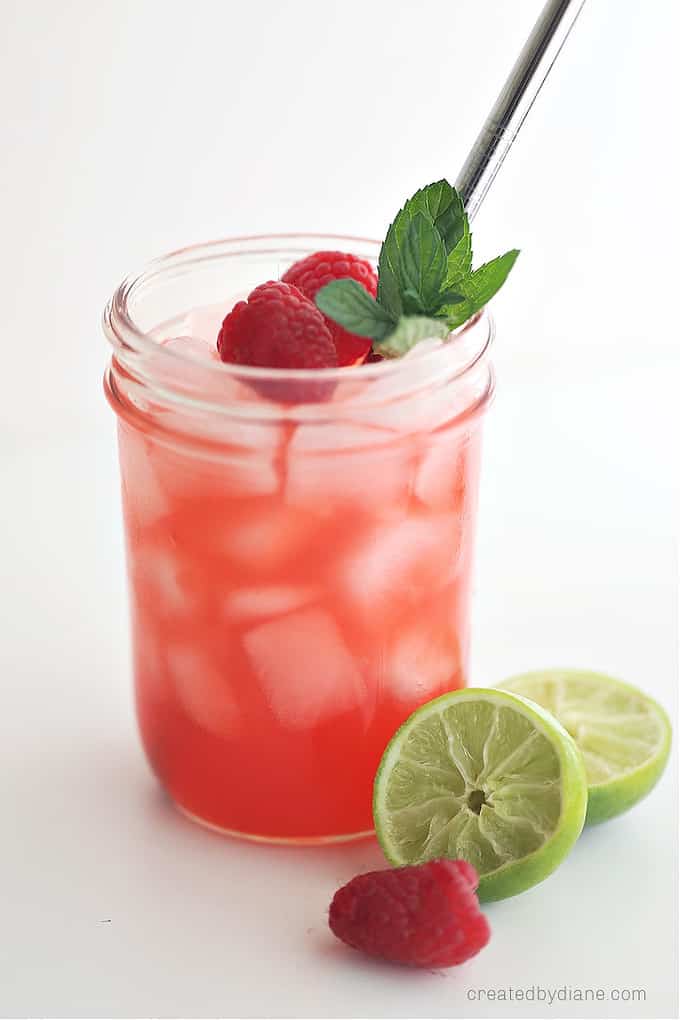 mason jar glass filled with raspberry drink, ice, margarita, mint leaves, straw, raspberry, lime wedge createdbydiane.com